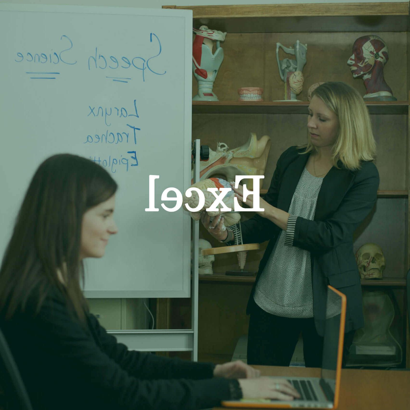照片中的教授和一个学生拿着一台笔记本电脑，上面的文字覆盖着“Excel”."